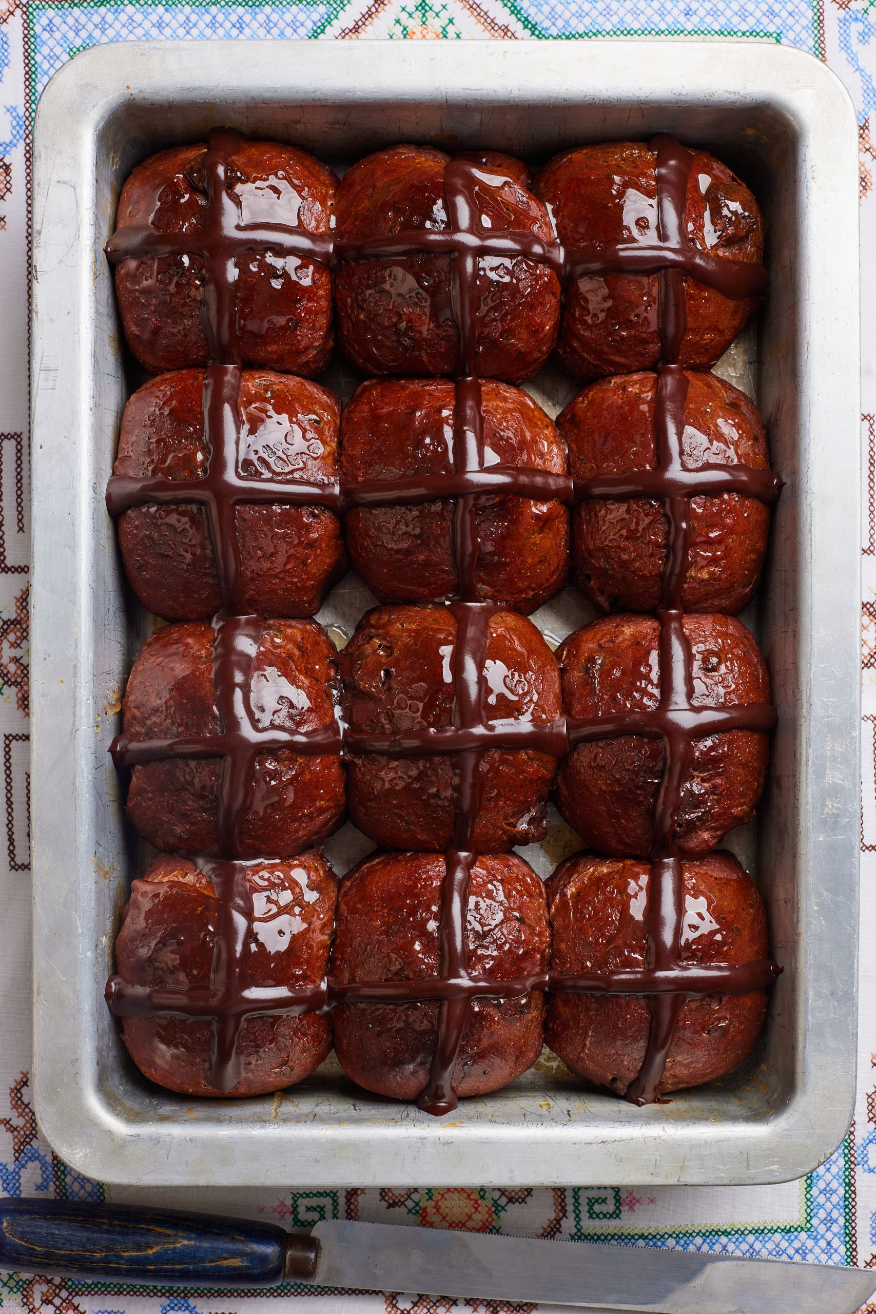 A top-down view of a tray of shiny fluffy Chocolate Hot Cross Buns. 