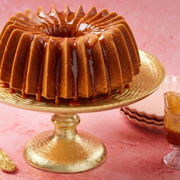 A whole Whiskey Cake on a cake stand shows its golden brown color, moist fine crumb and glossy glaze.