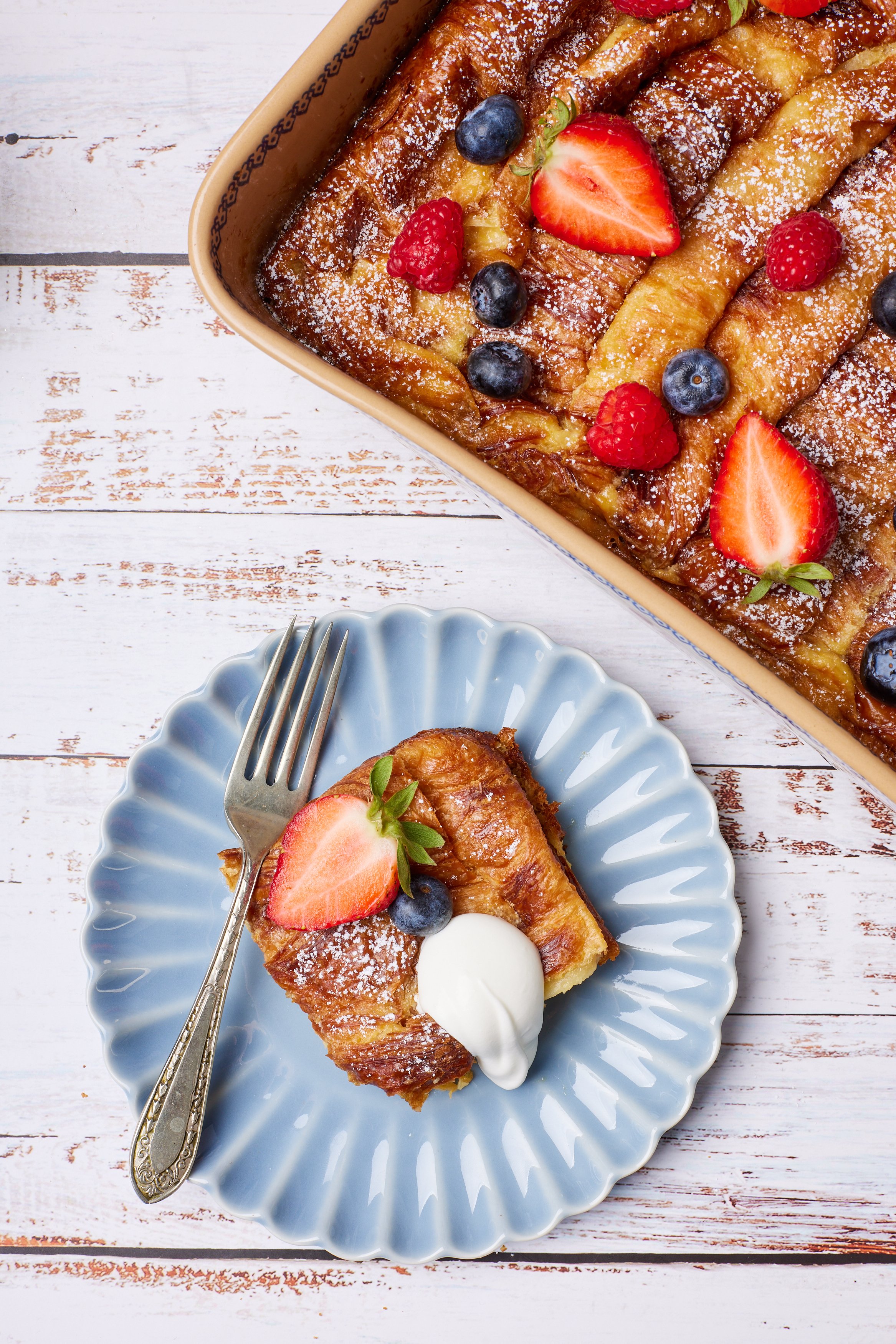 A square of French Toast Croissants Casserole is served on a dessert plate with softly whipped cream .