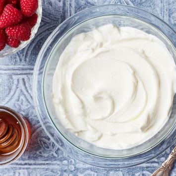 Top down view of a bowl of homemade Greek Yogurt, with a bowl of raspberries and honey on the side .