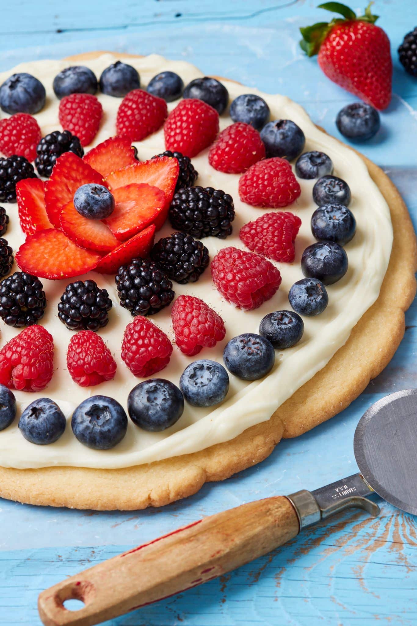 A close-up shot at the July 4th Fruit pizza shows the sugar cookie crust with spread and fresh blueberries and strawberries.