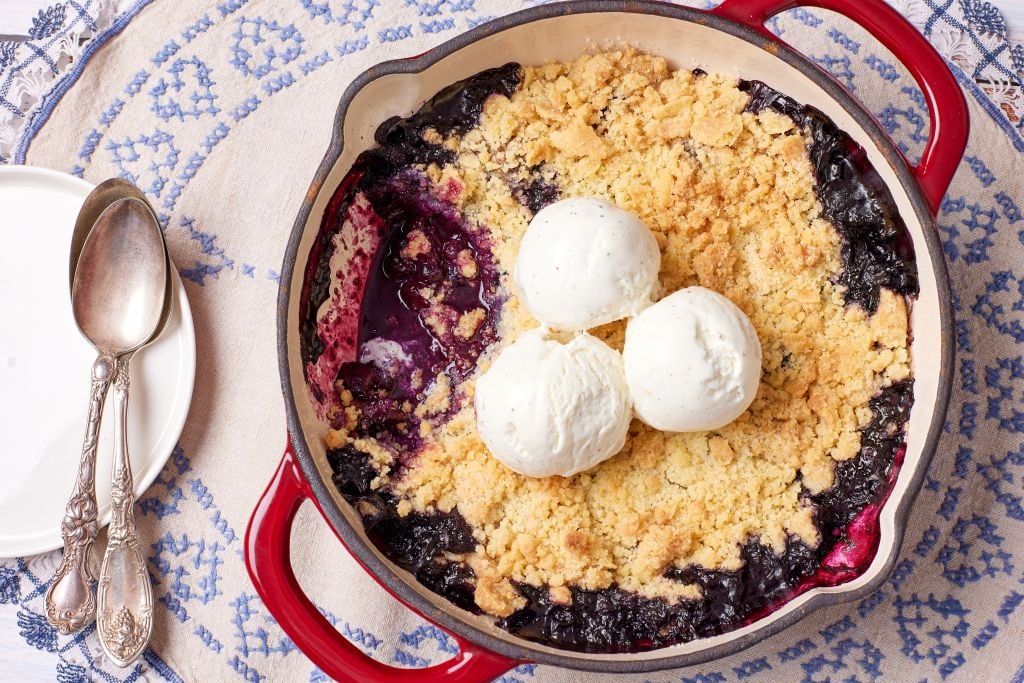 A top-down view of blueberry cobbler with golden topping, juicy blueberries and ice cream
