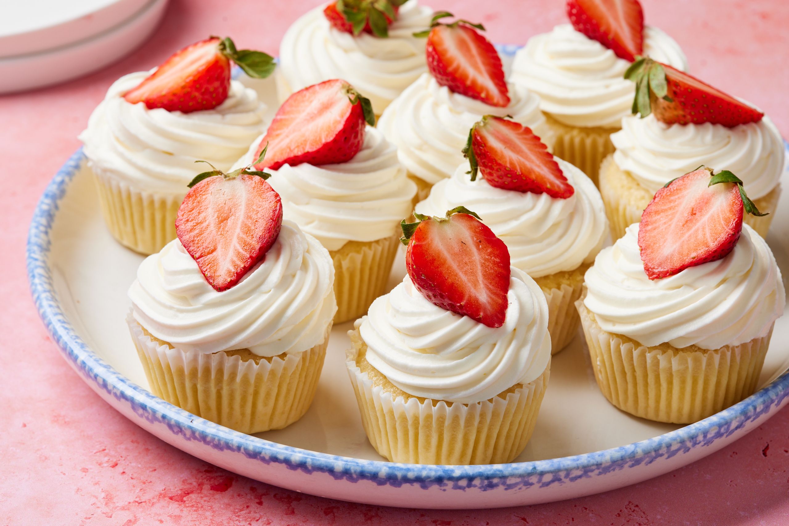 A plate of Strawberry Shortcake Cupcakes topped with velvety mascarpone whipped cream frosting and fresh straberry slice.