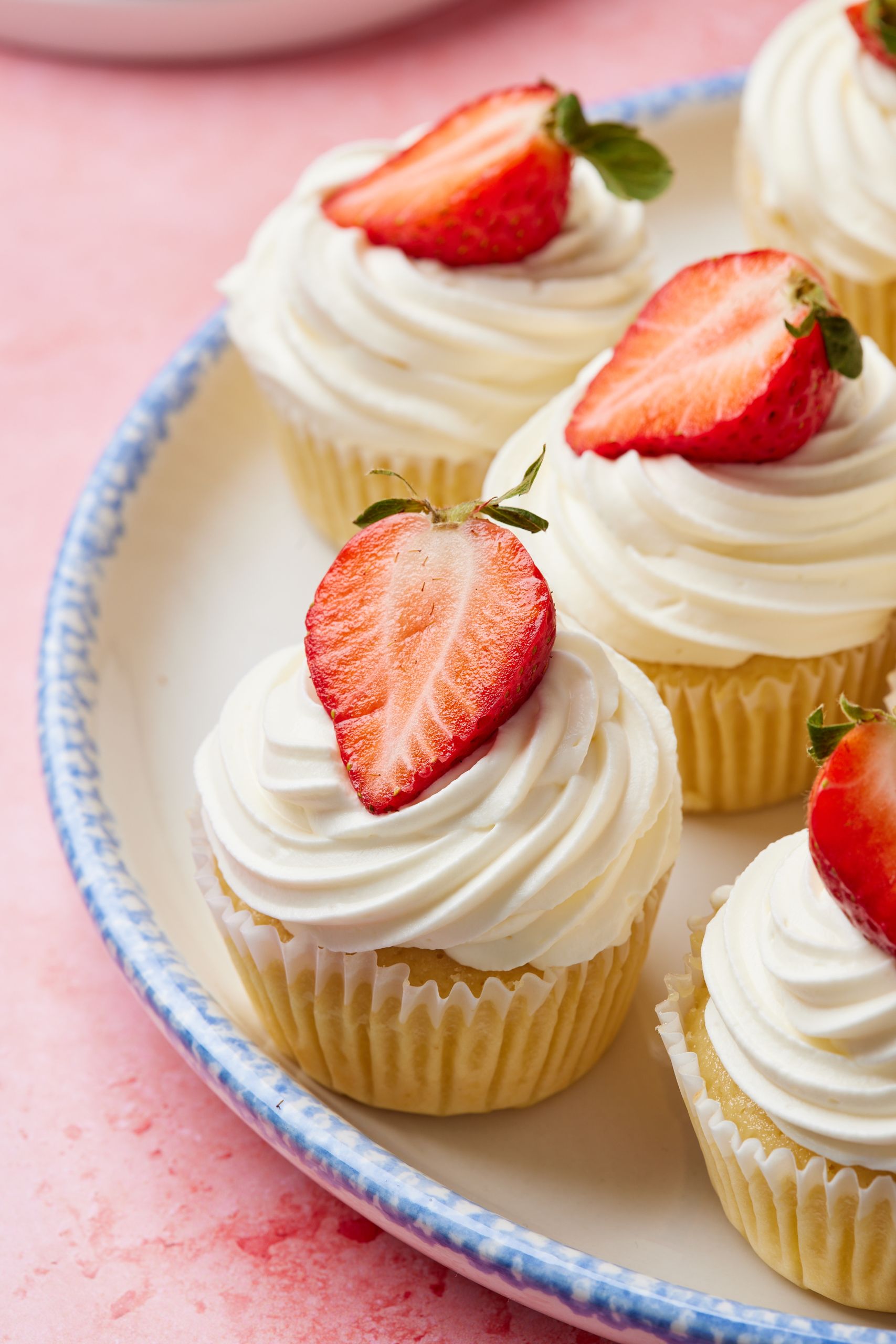 Close-up shot at strawberry shortcake cupcakes shows the smooth frosting on top with fresh strawberry slices. 