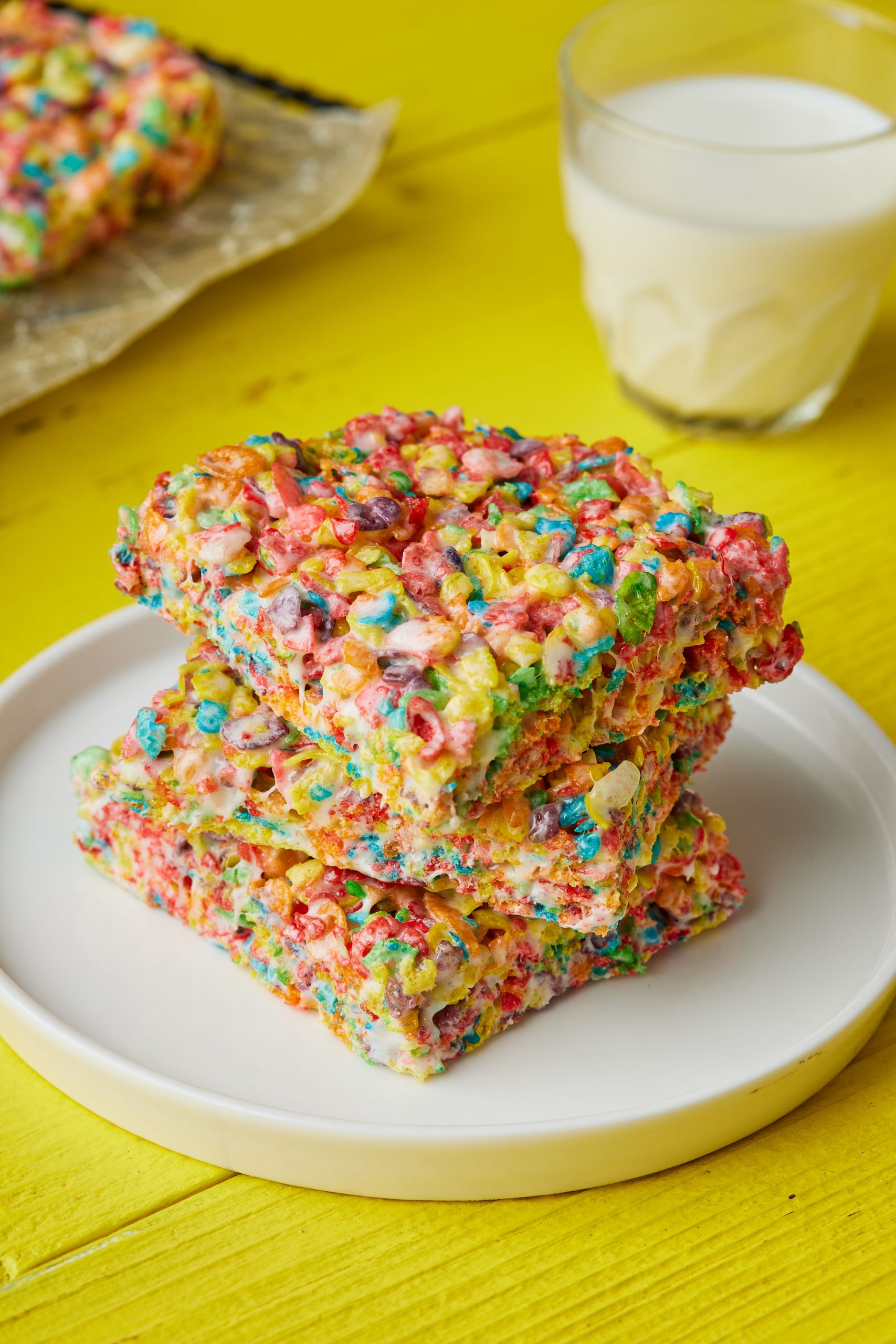 A stack of Fruity Pebbles Rice Krispie treats served with milk on the side. 
