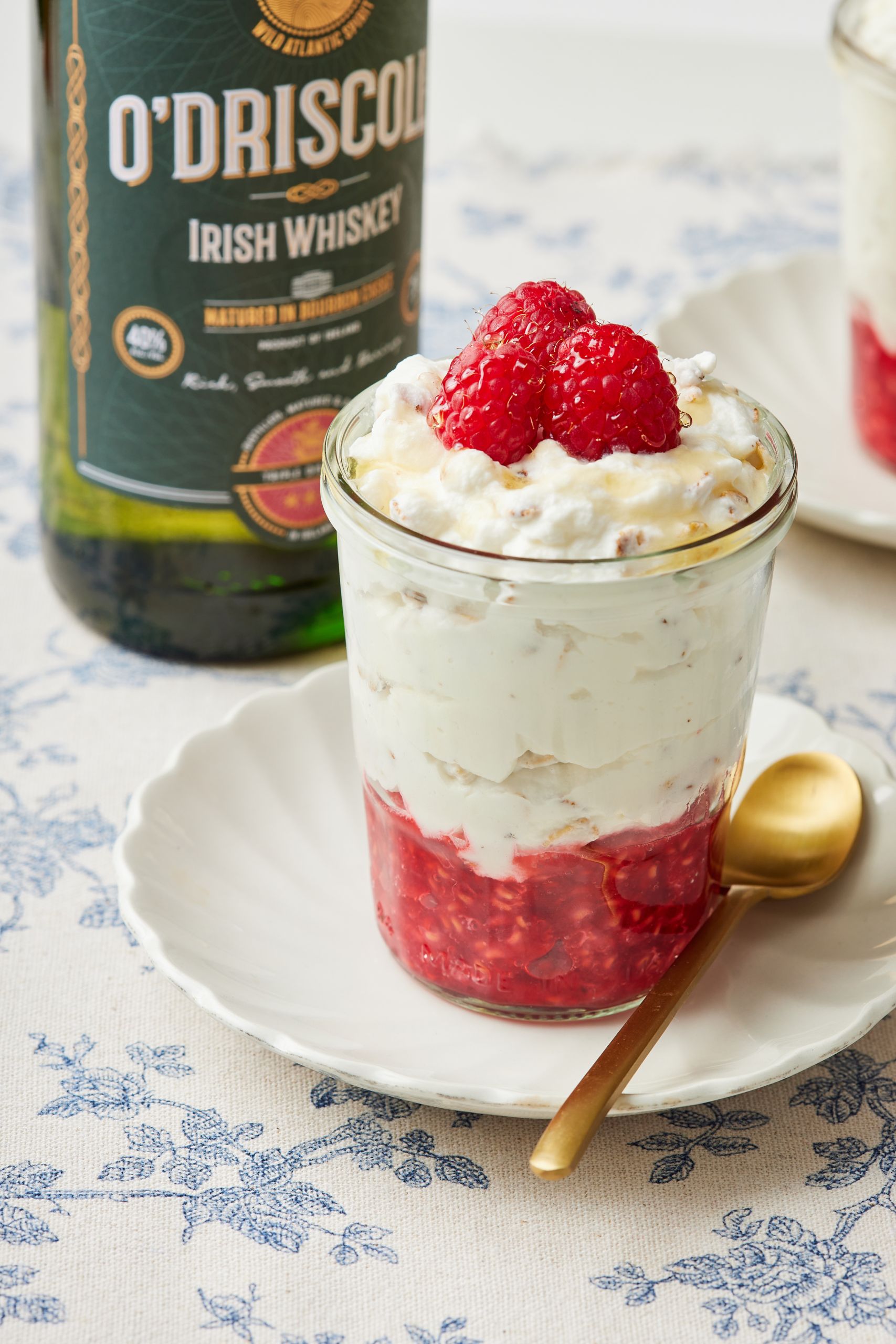 Cranachan is served with fresh raspberries on top. A bottle of Irish Whiskey is behind it. 