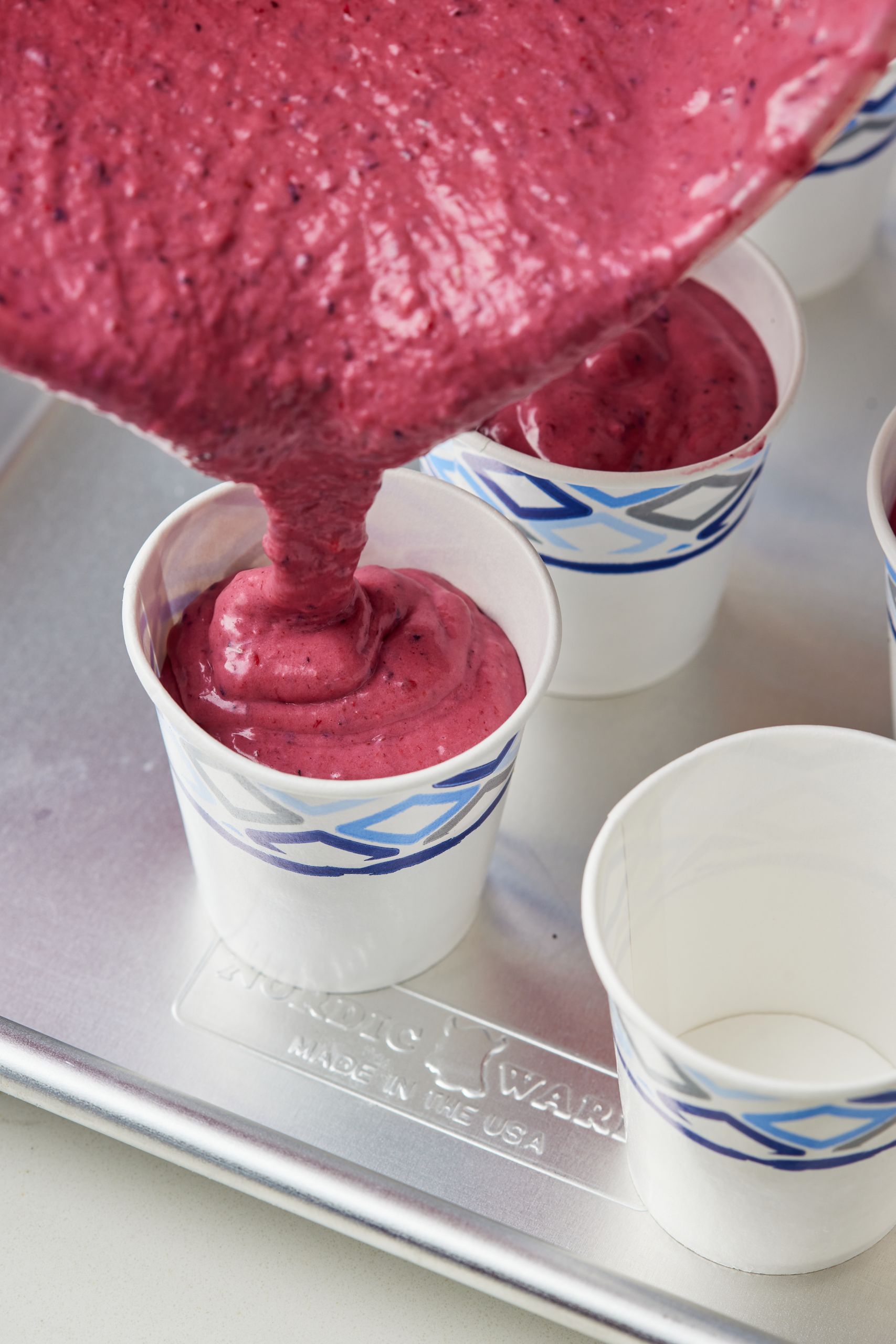 Step-by-step instructions on how to make pupsicles: pour the god popsicle mixture into cups.