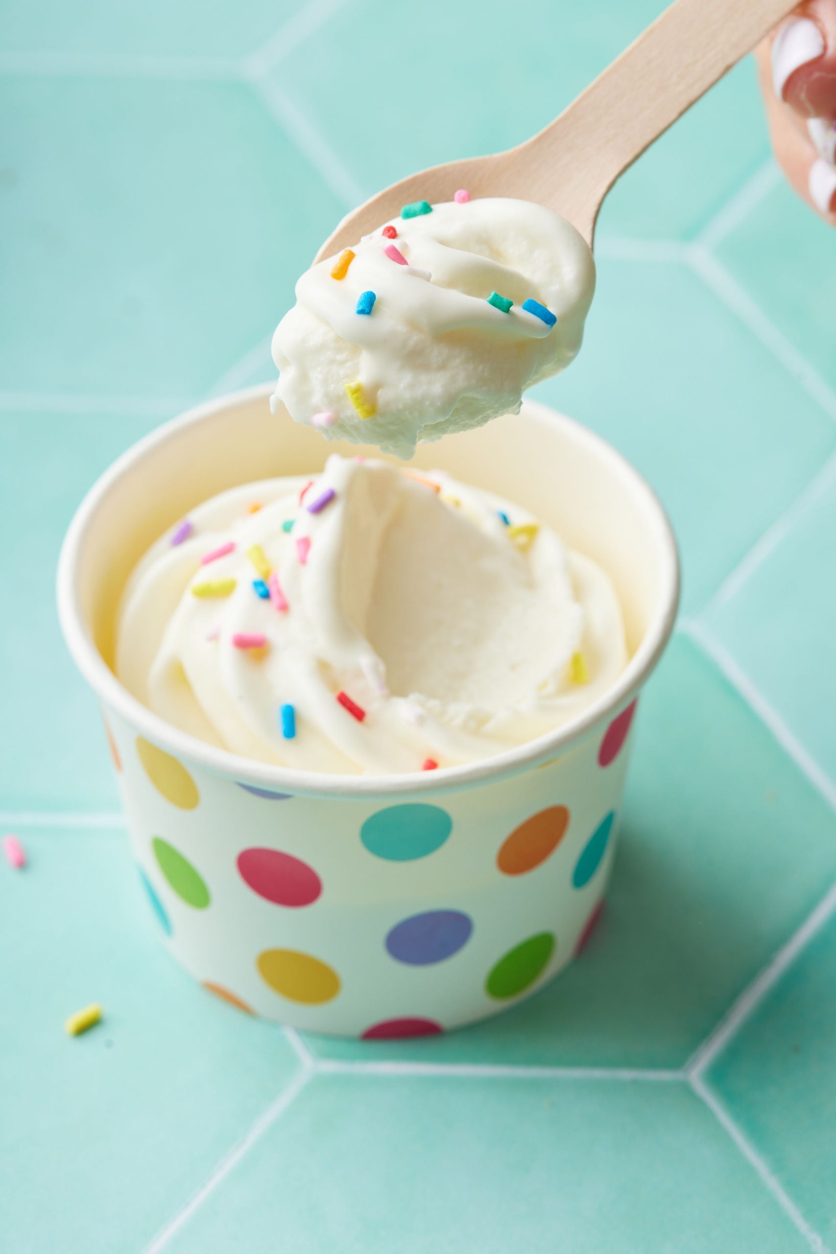A cup of soft serve frozen yogurt decorated with sprinkles issuing taken one scoop.