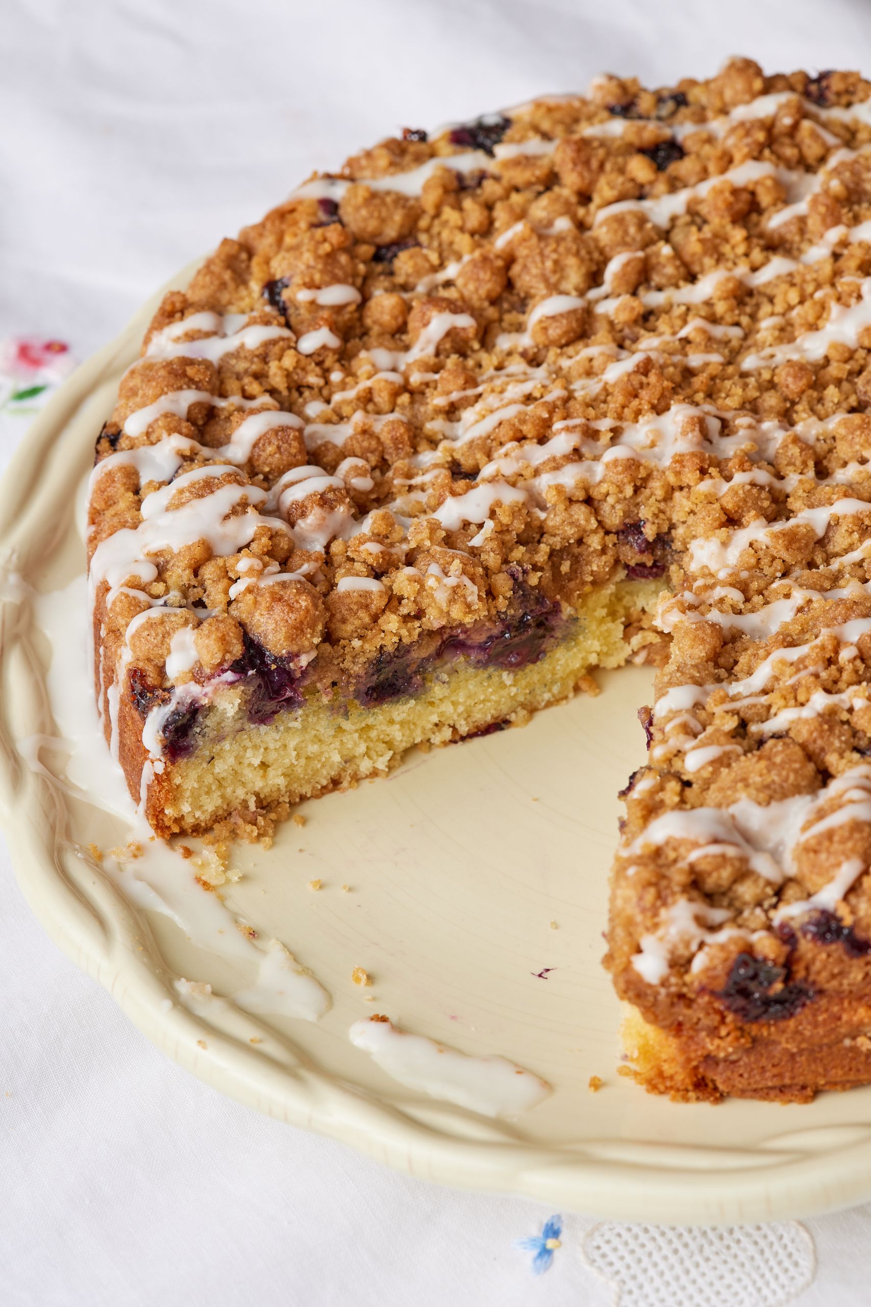 A whole coffee cake drizzled with glaze with one slice taken. 