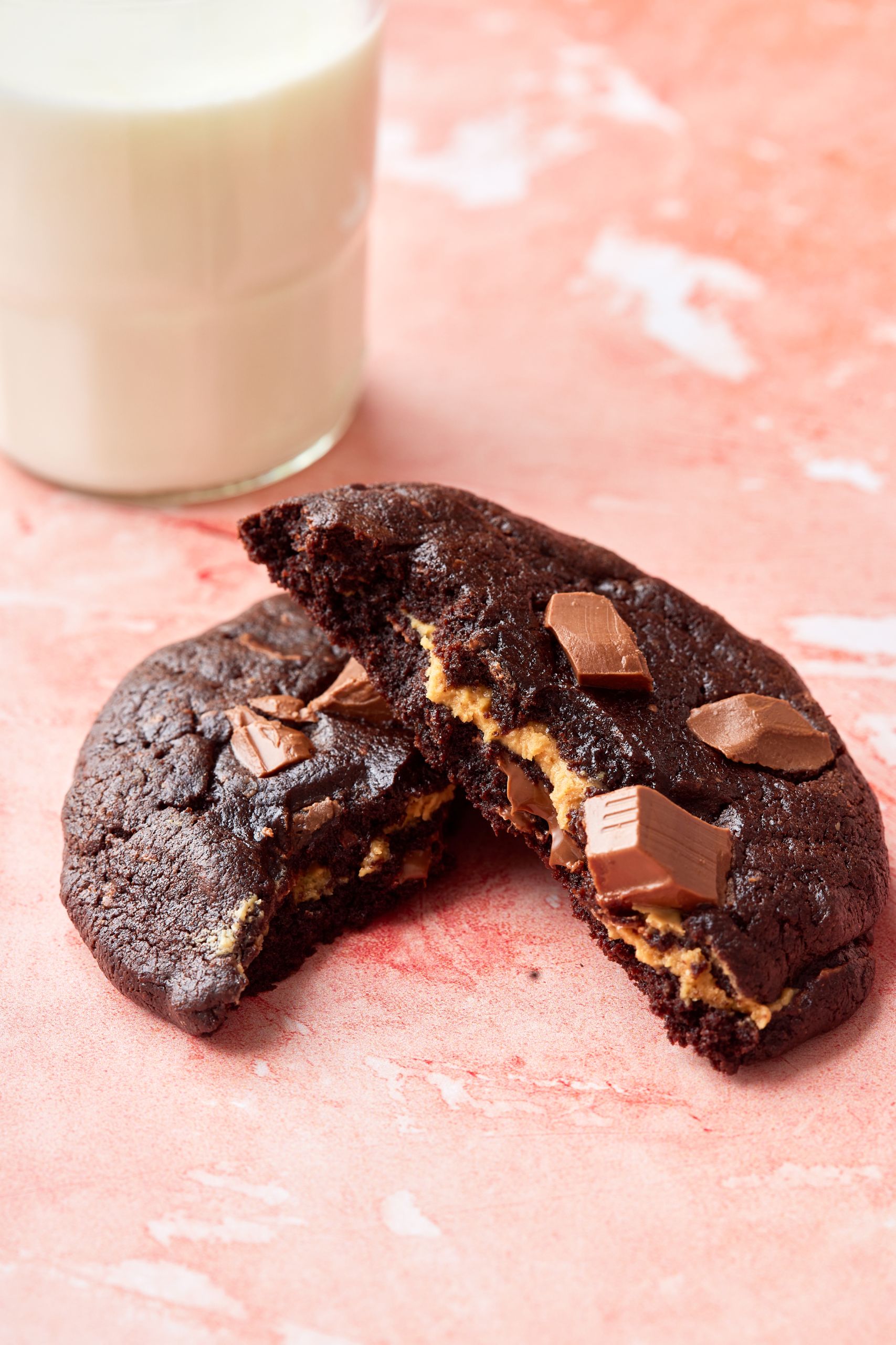 One cookie is split into halves and served with a glass of milk.