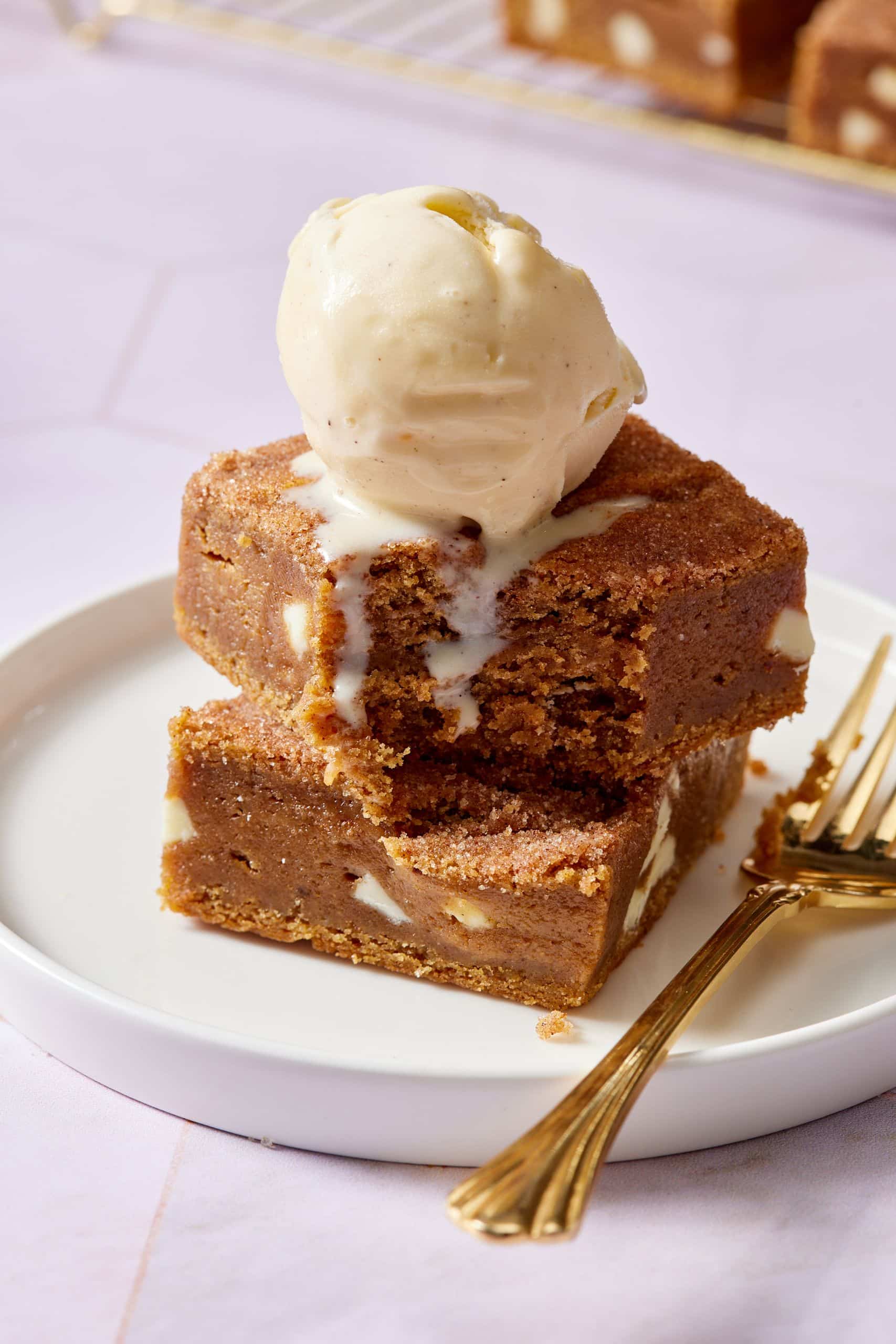 Two squares of pumpkin blondies stacked together and served with ice cream on top. One bite is take from the top piece. 