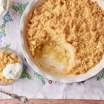 A top-down view of golden apple cobbler with one part scooped out & served in a small bowl.