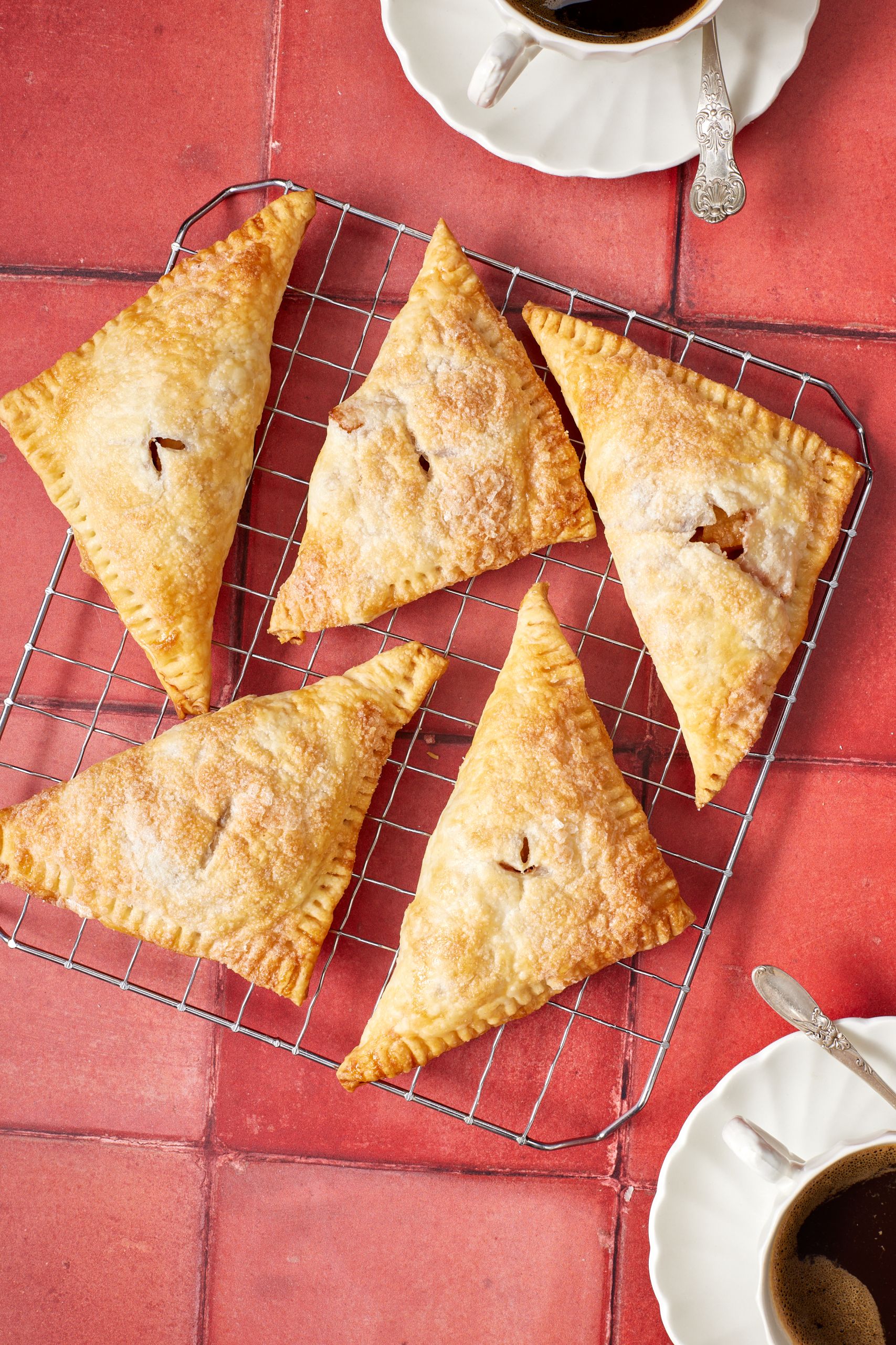 Golden apple turnovers on the cooling rack, served with coffee on the side.