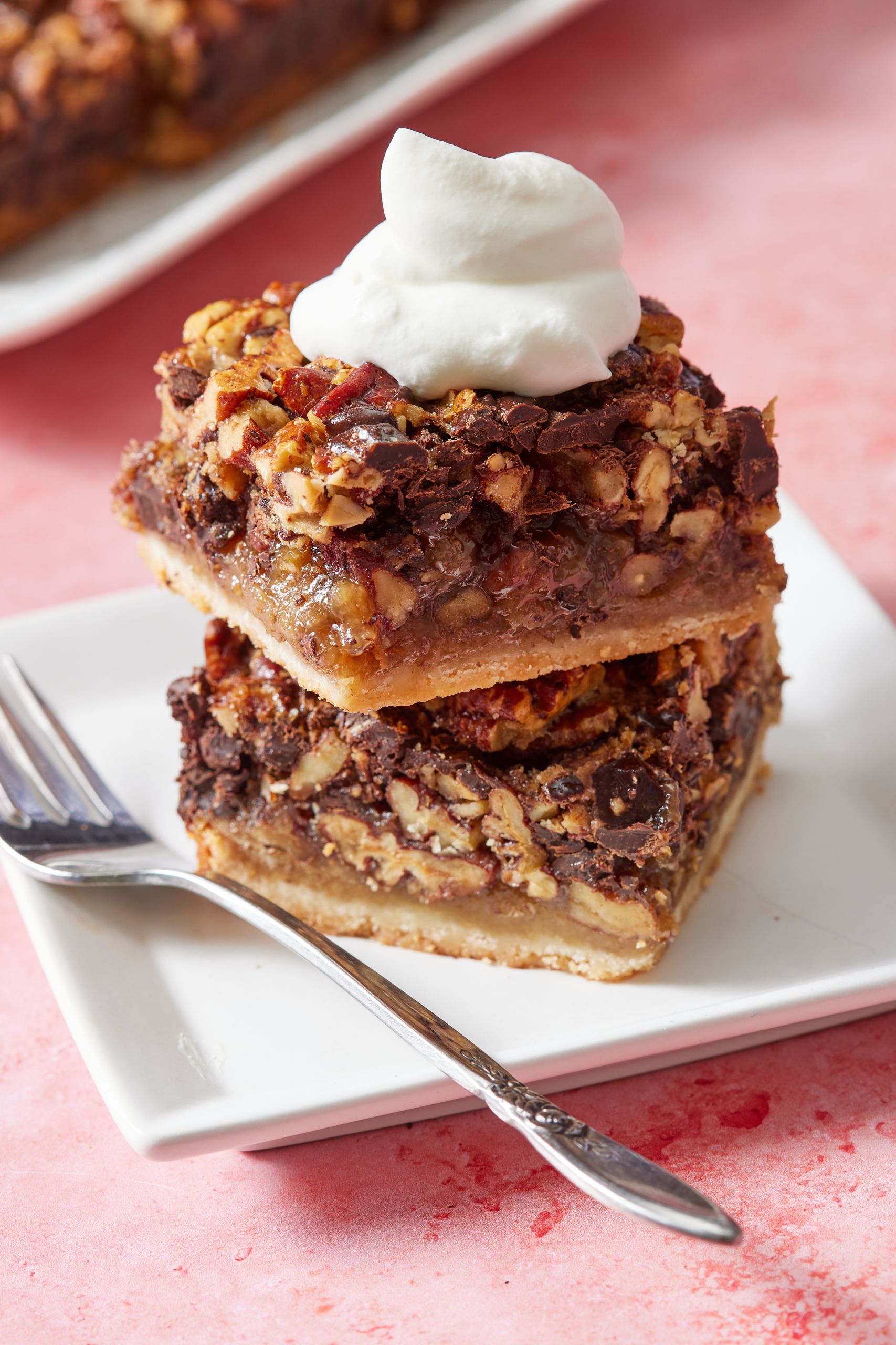 Two squares of chocolate pecan pie bars stacked together served with softly-whipped cream on top.