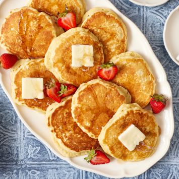 Top down view of a platter of golden fluffy maple pancakes served with butter, starwberries and coffee.