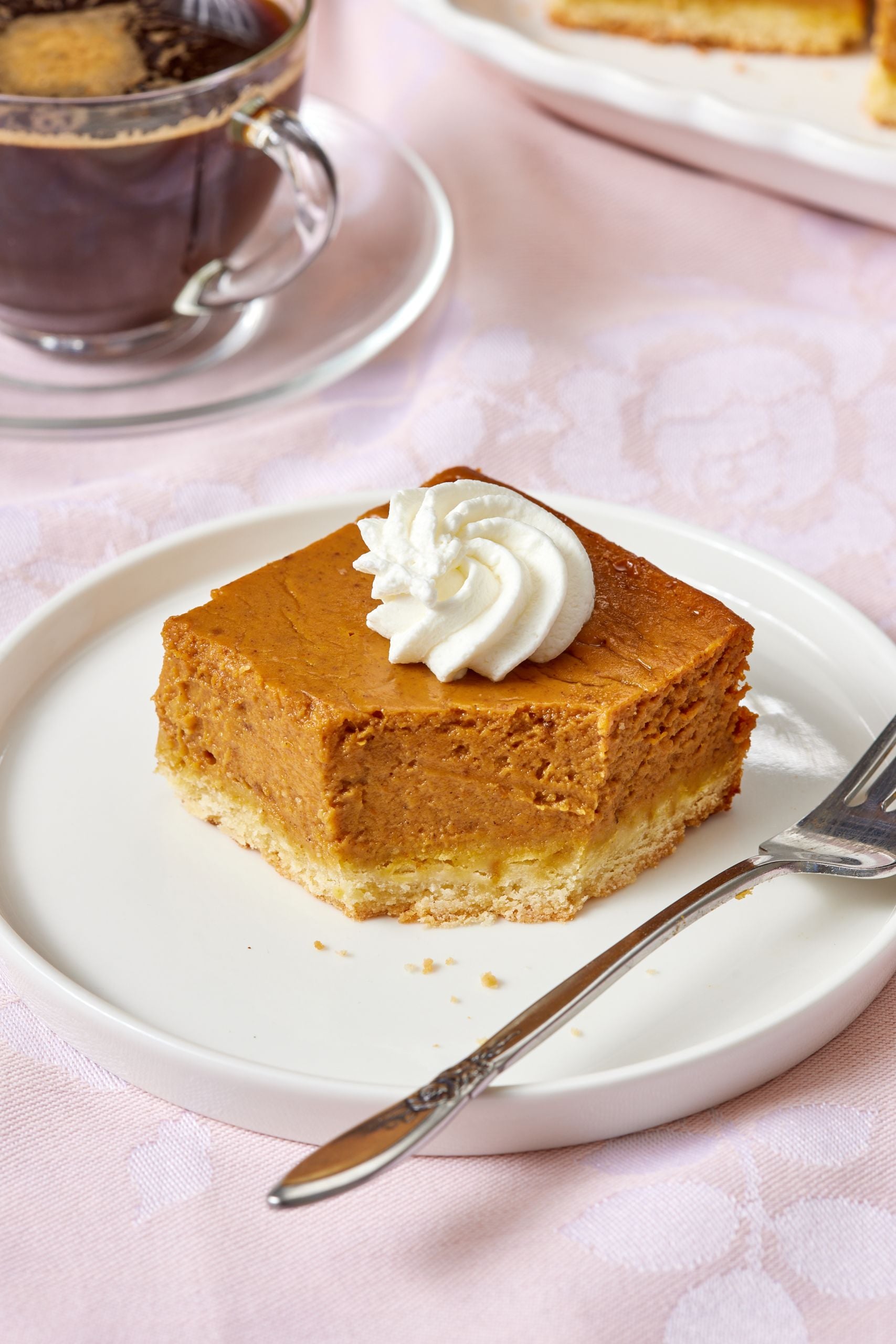 A square of Pumpkin Pie Bars served with whipped cream on top and has one bite taken. Coffee is served in the side. 