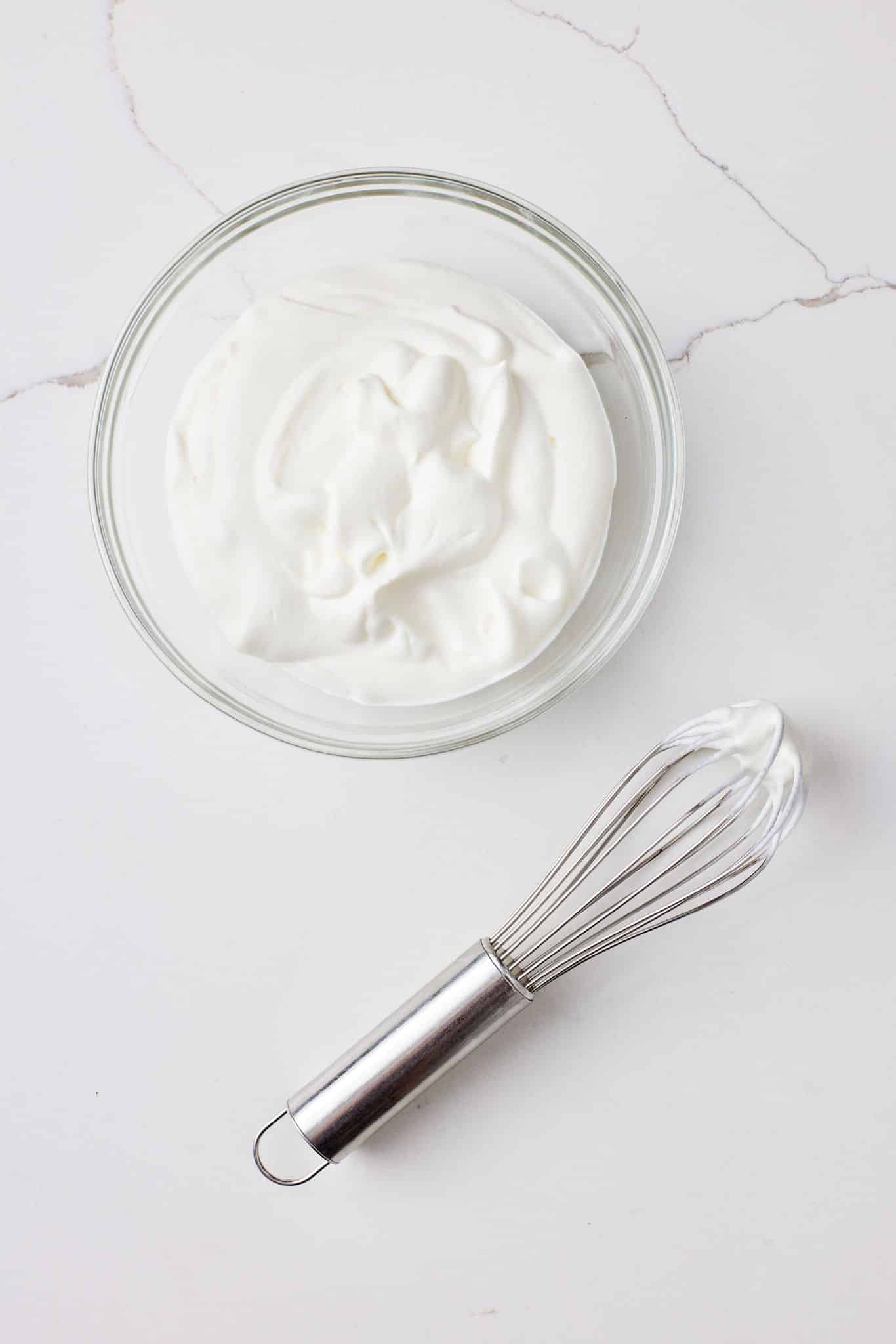 A bowl of whipped cream for French Silk Pie filing with a whisk next to it. 