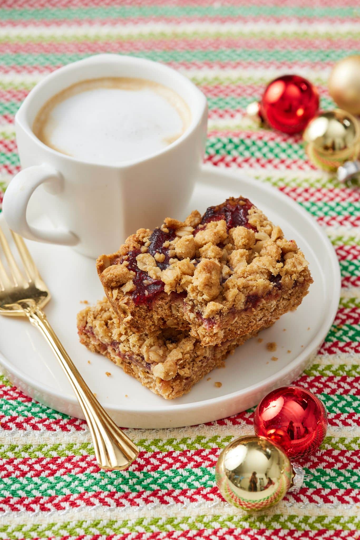 Two pieces of Cranberry Oatmeal Bars served on a plate with a cup of coffee. 