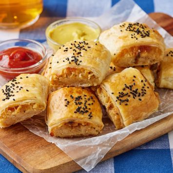 Golden flaky Cheese and Onion Rolls served on a wooden board with ketchup and Dijon mustard.