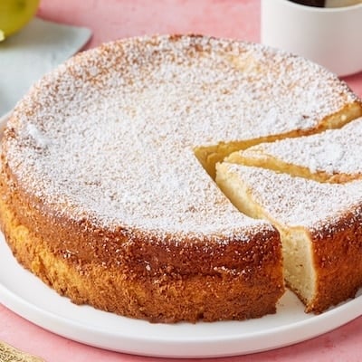A lemon ricotta cake dusted with powdered sugar and served with two cups of coffee on the side.