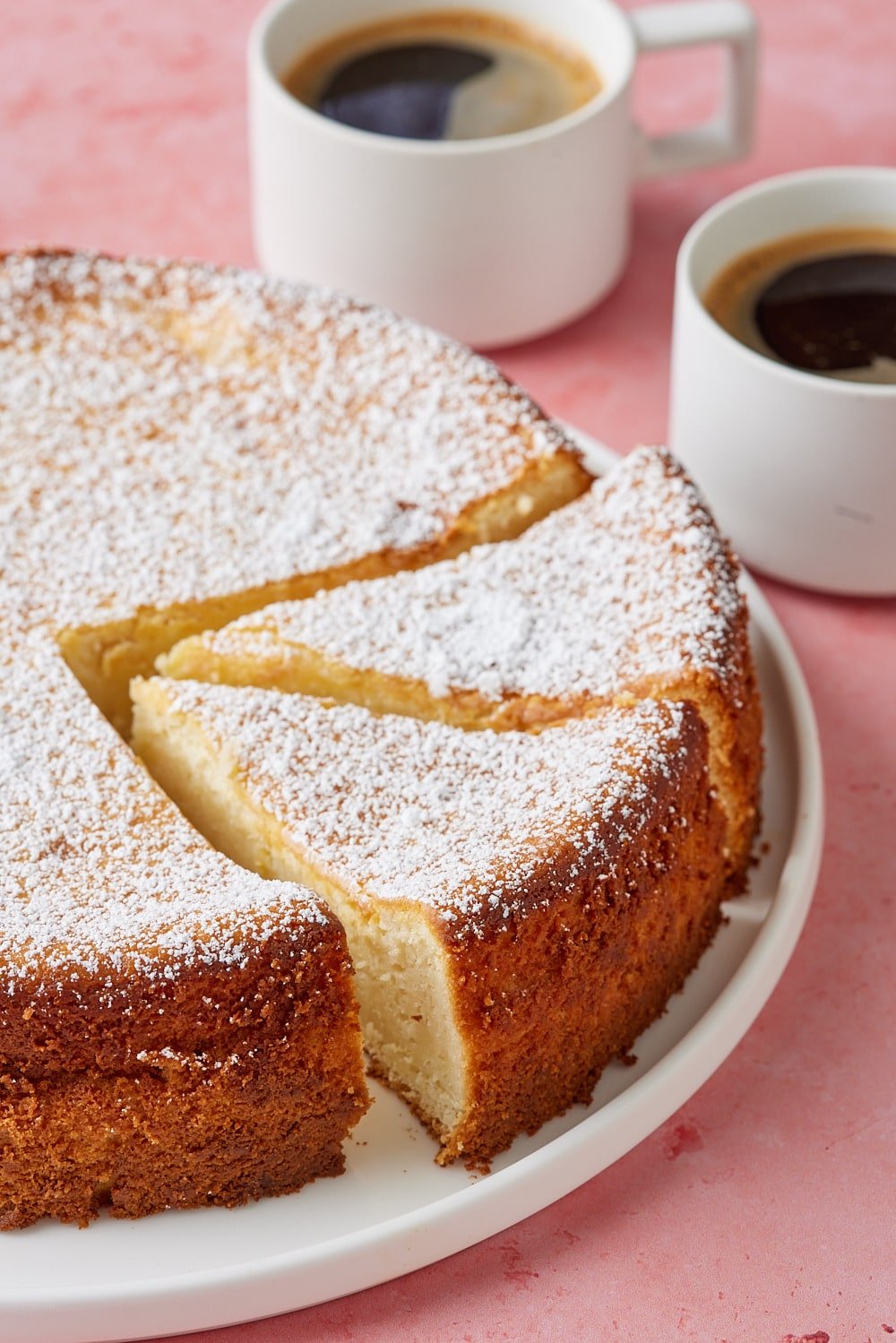 Lemon Ricotta Cake9 A lemon ricotta cake dusted with powdered sugar and served with two cups of coffee on the side.