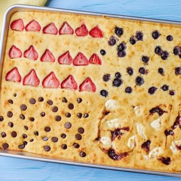 Sheet Pan Pancakes with strawberries, blueberries, chocolate chips, and jam with cream cheese toppings.
