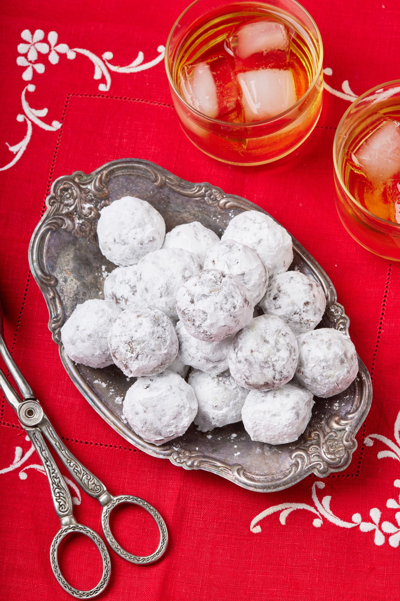 A platter of Whiskey Balls coated with powdered sugar, served with two glass of whiskey on the side.