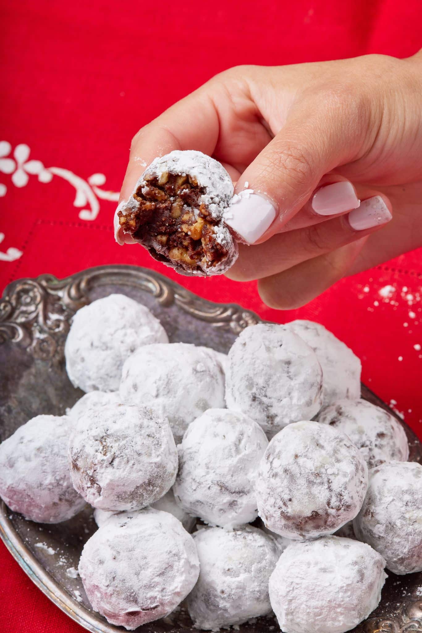 A whiskey ball above a plate with one bite taken , showing the fudgy inside. 