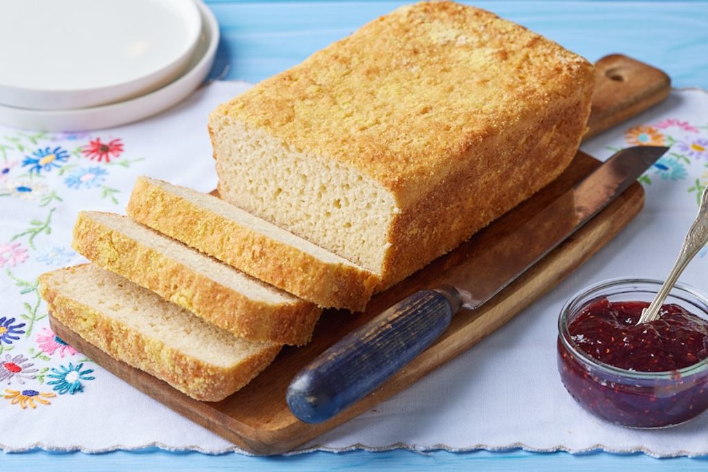 Three slices the rest of a loaf of golden English Muffin Bread on a wooden board, showcasing the airy nooks and crannies in the crumb.