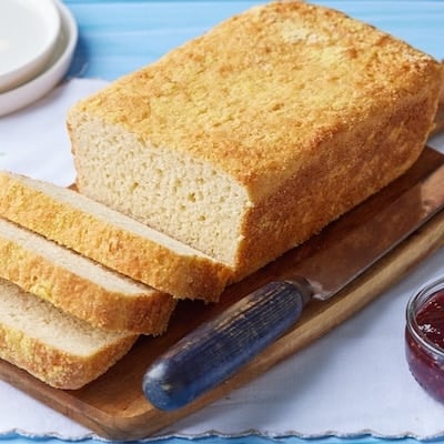 Three slices the rest of a loaf of golden English Muffin Bread on a wooden board, showcasing the airy nooks and crannies in the crumb.