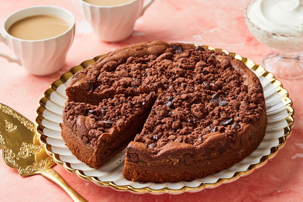 A chocolate coffee cake with a slice cut. Served with tea on the side.