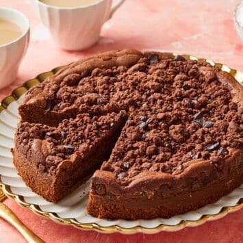 A chocolate coffee cake with a slice cut. Served with tea on the side.