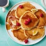 Topdown view of a plate of fluffy lemon pancakes served with fresh berries on top and coffee on the side