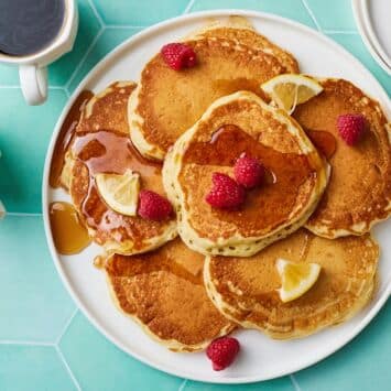 Topdown view of a plate of fluffy lemon pancakes served with fresh berries on top and coffee on the side