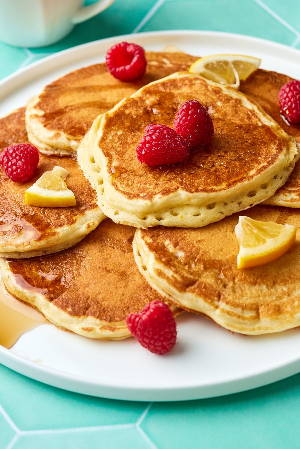A plate of golden fluffy lemon pancakes served with fresh raspberries and syrup. 