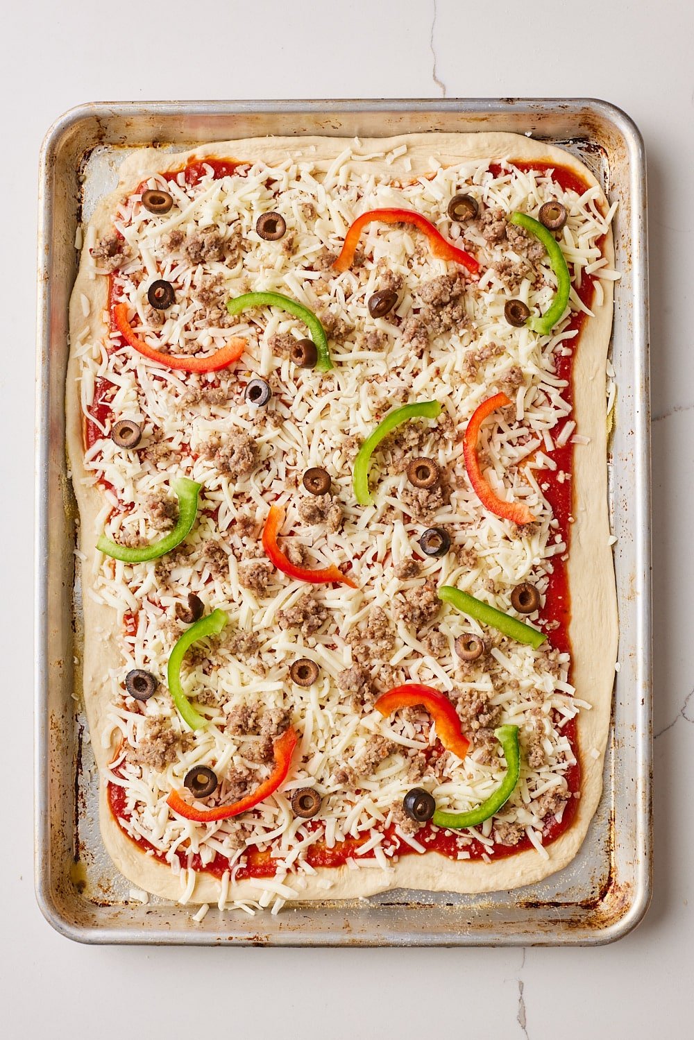 Sheet Pan Pizza6 Sheet Pan Pizza dough in the pan finished with toppings including peppers, sausage, olives.