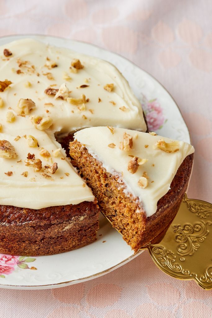 A slice of small carrot cake is being cut and lifted away from the whole cake.