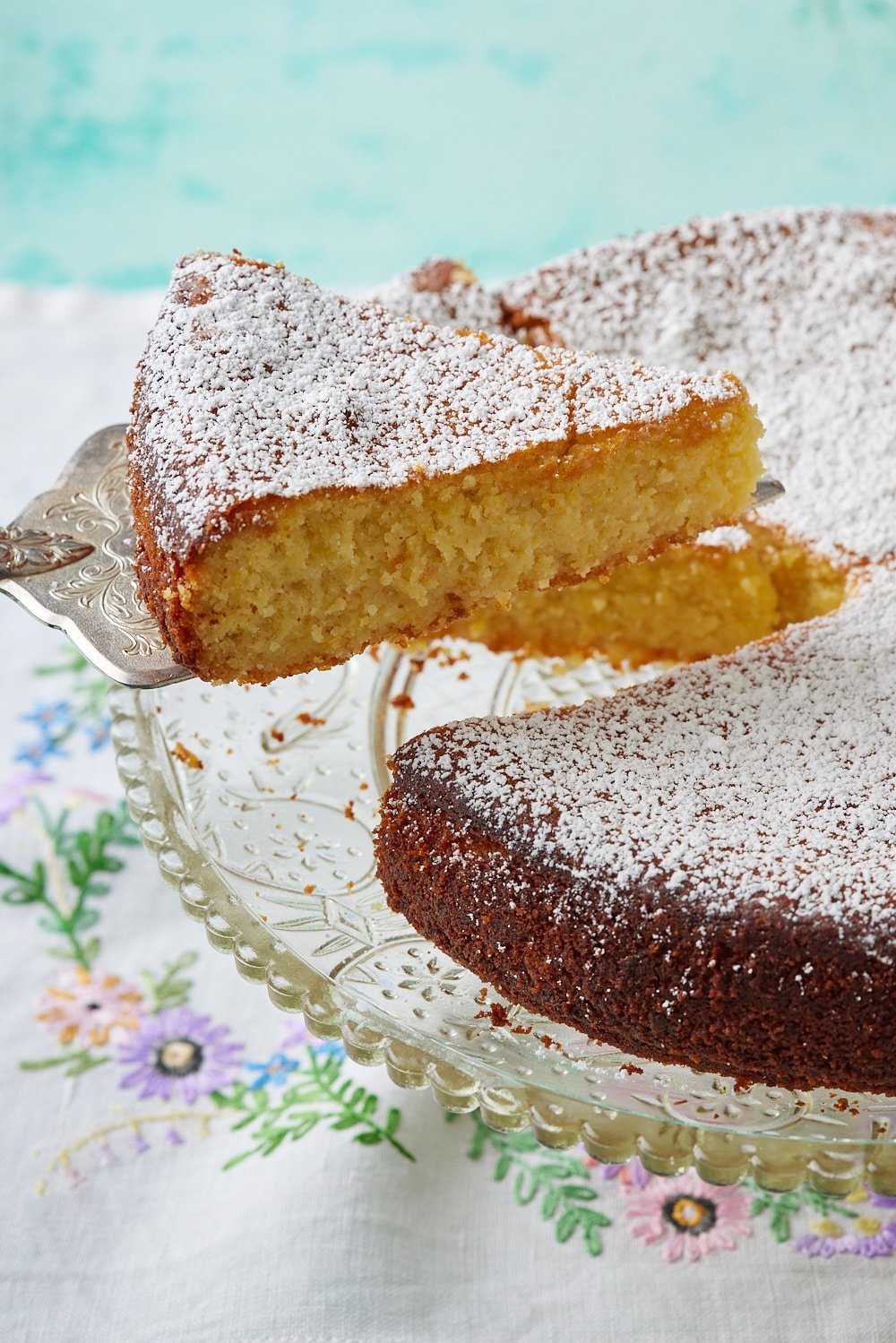 Torta Caprese Bianca10 A slice of torta caprese is cut and being lifted from the cake on th stand.