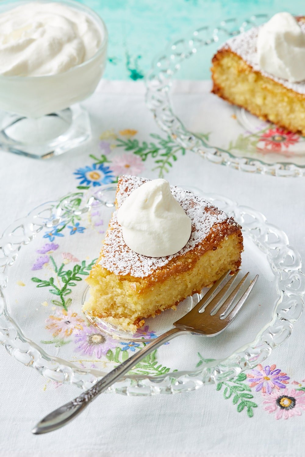 Torta Caprese Bianca12 Two slices of lemon torta caprese are served with whipped cream. One slice has one bite taken.