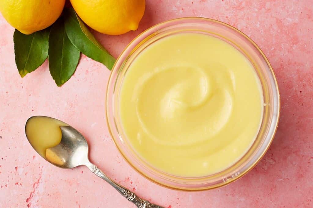 Top-down view of a lemon recipe-a bowl of lemon curd with fresh lemons on the side.