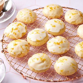 Lemon Ricotta Cookies with glossy glaze and lemon zest on the wire rack. Served with two cups of tea on the side.