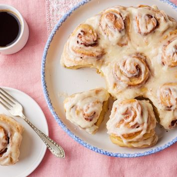 Top-dwon view of Sourdough Cinnamon rolls with cream cheese glaze. One roll is served separately on a plate and served with coffee.