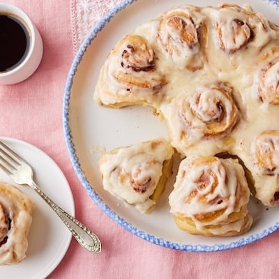 Top-dwon view of Sourdough Cinnamon rolls with cream cheese glaze. One roll is served separately on a plate and served with coffee.