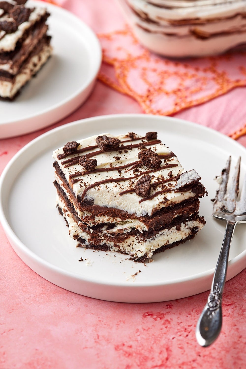 Two pieces of layered chocolate icebox cake served on dessert plates, with one bite taken. The remaining cake in the pan.