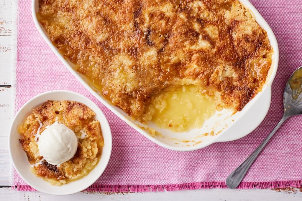 Top-down view of golden pineapple dump cake in a baking dish. One scoop is served with ice cream.