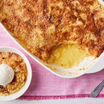 Top-down view of golden pineapple dump cake in a baking dish. One scoop is served with ice cream.