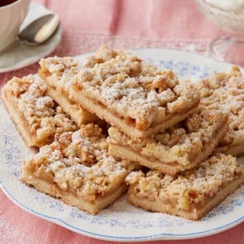 A plate of Apple Crumble Bars dusted with powdered sugar, served with coffee on the side.