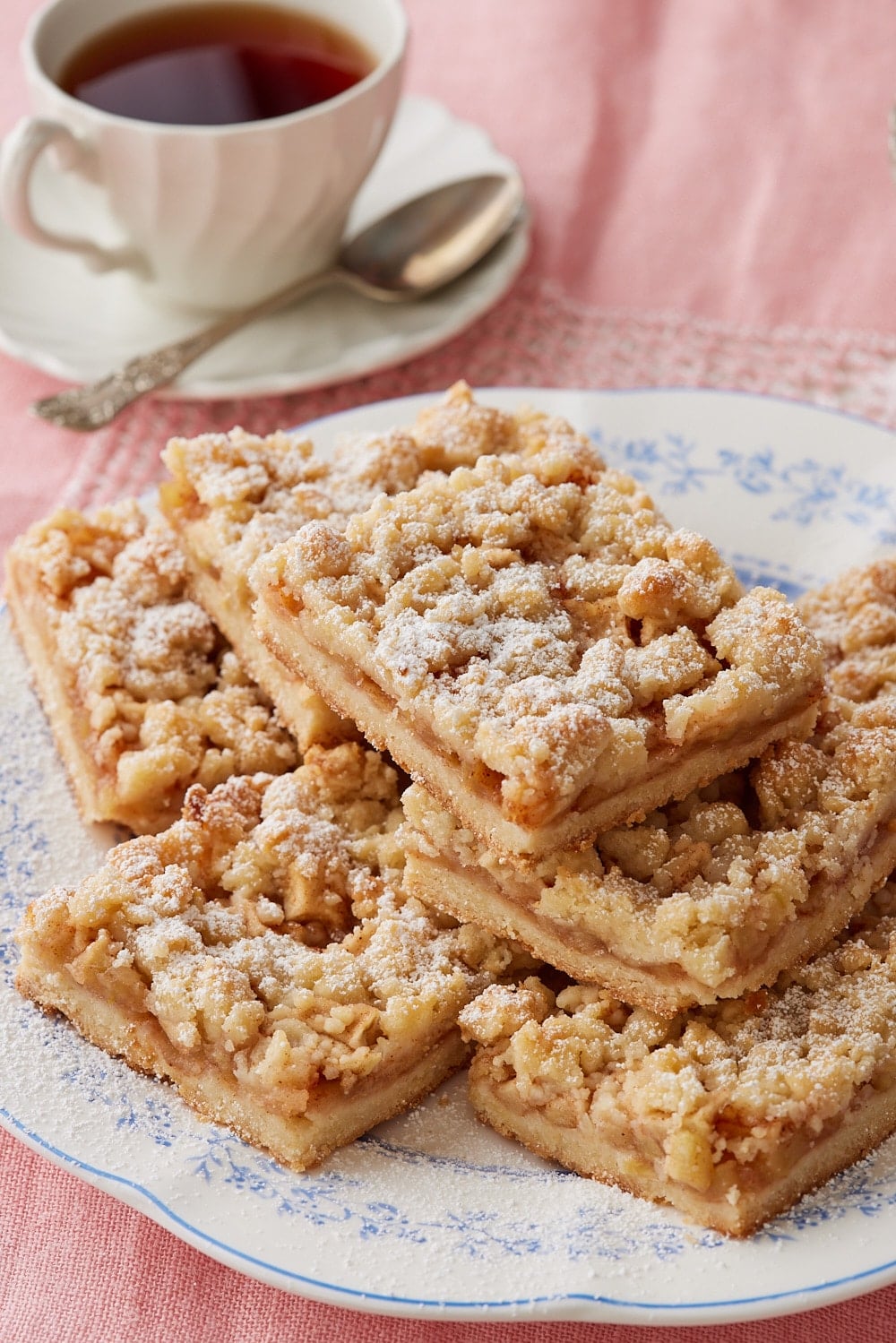 A plate of Apple Crumble Bars dusted with powdered sugar, served with a cup of coffee on the side. 