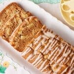 Whole Apple Loaf Cake drizzled with apple glaze and sliced to reveal a moist cinnamon-spiced crumb filled with diced apples on a white serving platter.