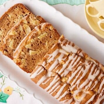 Whole Apple Loaf Cake drizzled with apple glaze and sliced to reveal a moist cinnamon-spiced crumb filled with diced apples on a white serving platter.